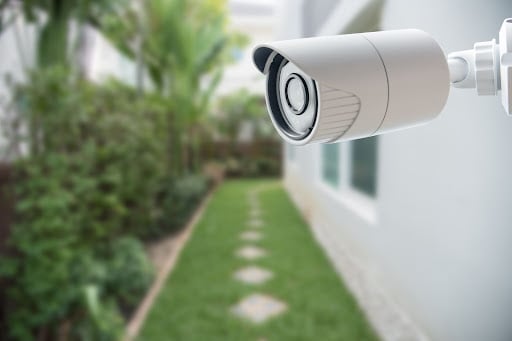 Una foto de una cámara de seguridad en la pared exterior de una casa que da al costado de la casa y al área del jardín.