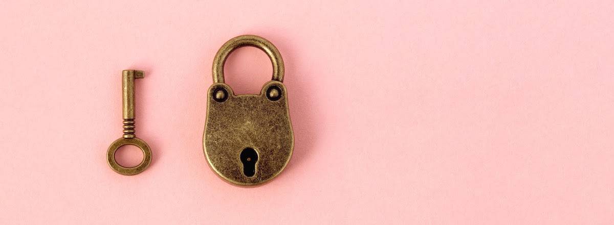 Un simple candado de latón junto a una llave a juego sobre un fondo rosa.