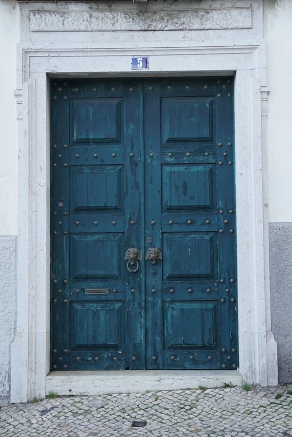 Un conjunto de puertas dobles de color verde azulado con aldabas en forma de león de hierro.