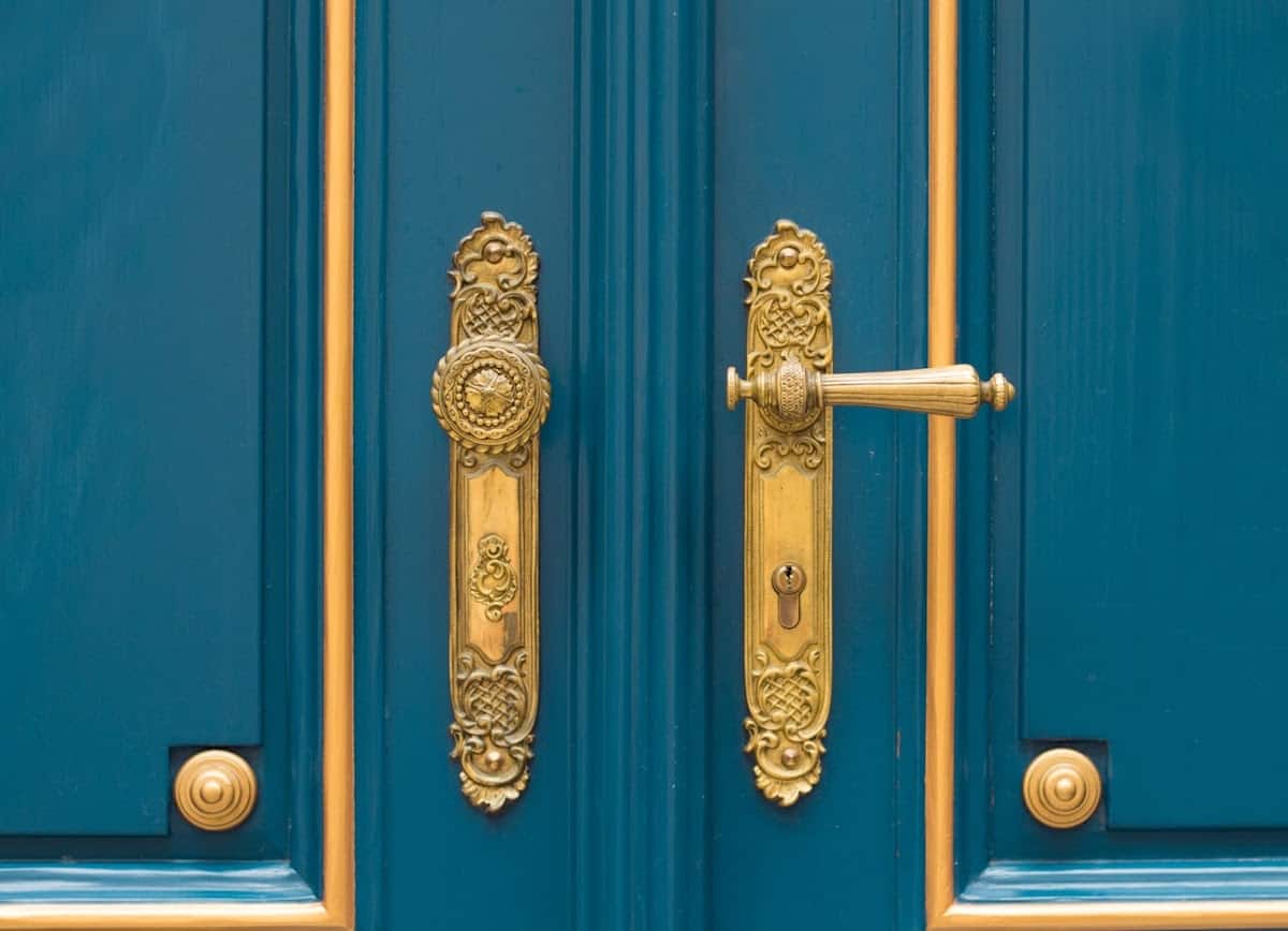 Pomos chapados en oro en puertas verde azulado con detalles dorados.