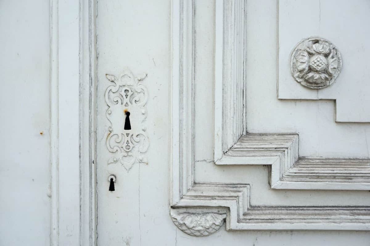 Cerradura pintada de blanco en una puerta blanca con detalles ornamentales.