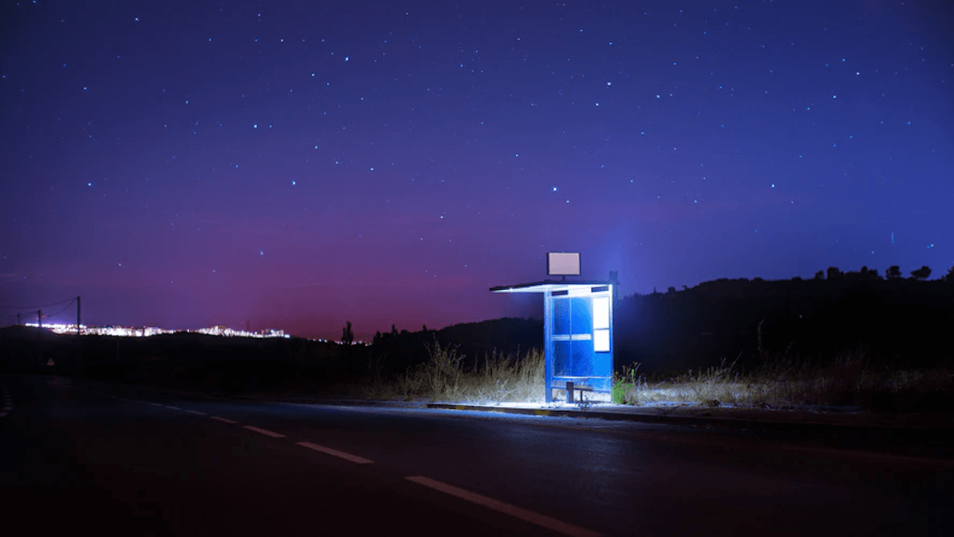 Una parada de autobús iluminada junto a la carretera por la noche.