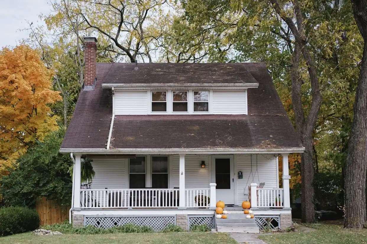 Una casa blanca en otoño con calabazas en el porche.