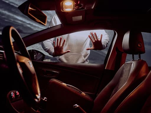 Las manos de una persona presionadas contra el exterior de la ventana de un automóvil.  No hay nadie dentro del coche, pero las luces están encendidas.  